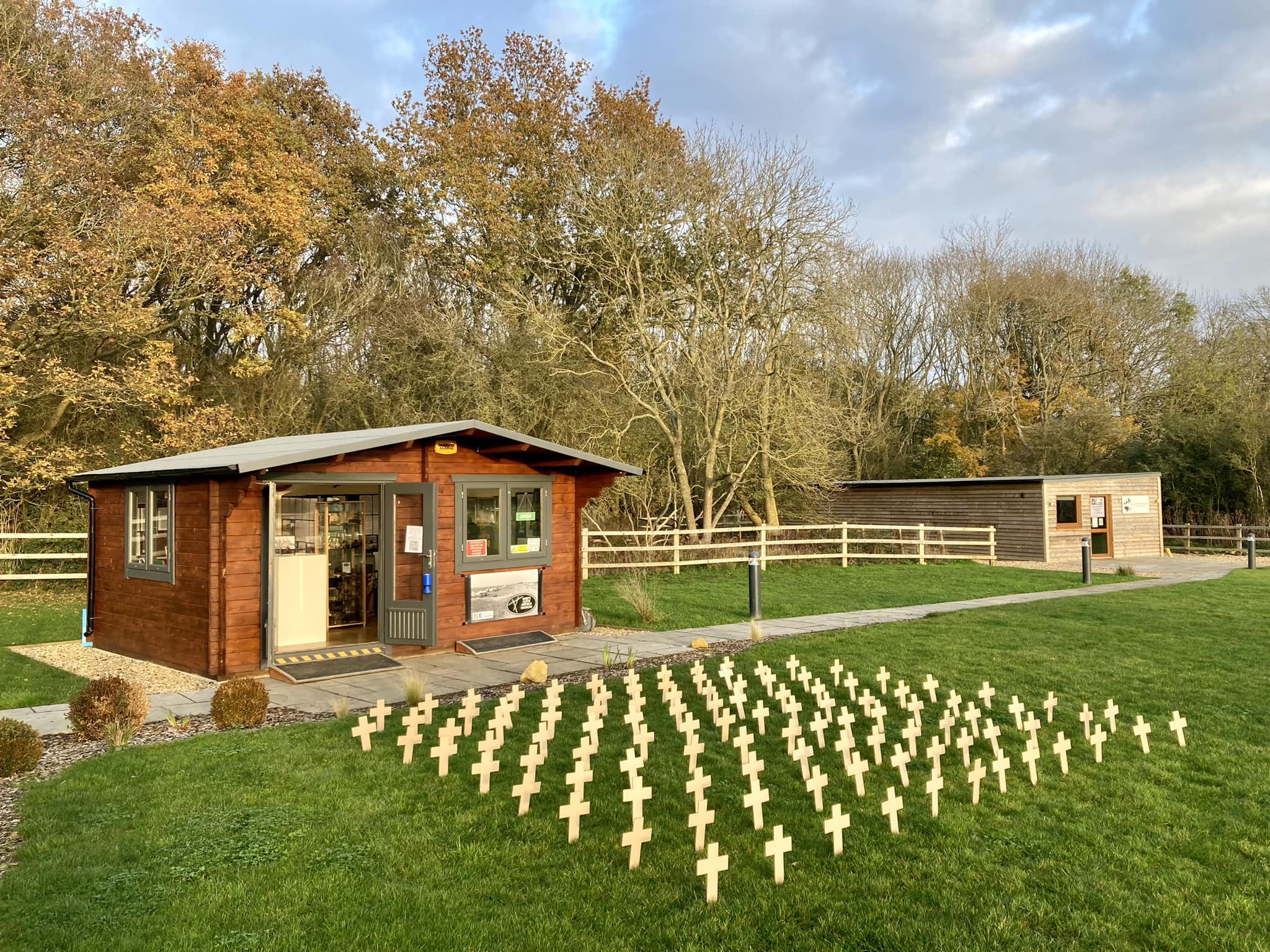 The Kings Cliffe Airfield Museum building, a small timber cabin with rows of small wooden remembrance crosses set out on the grass in front of it