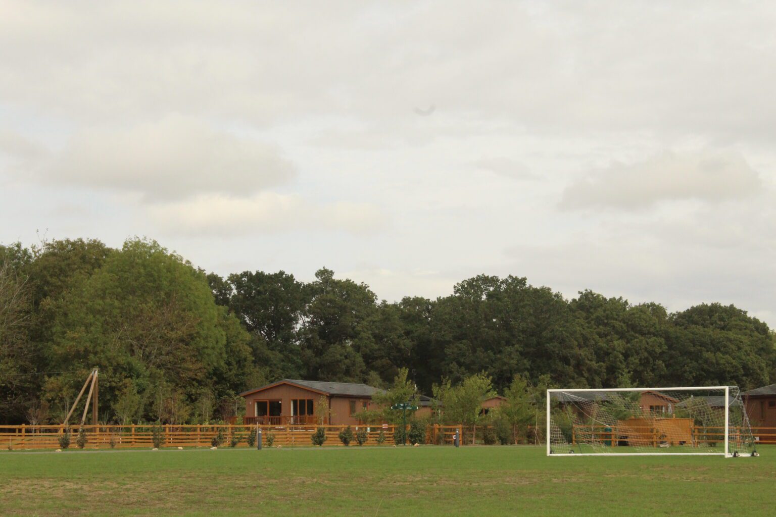 A full-size football goal on the green at Rockingham Forest Park, with lodges and mature woodland behind