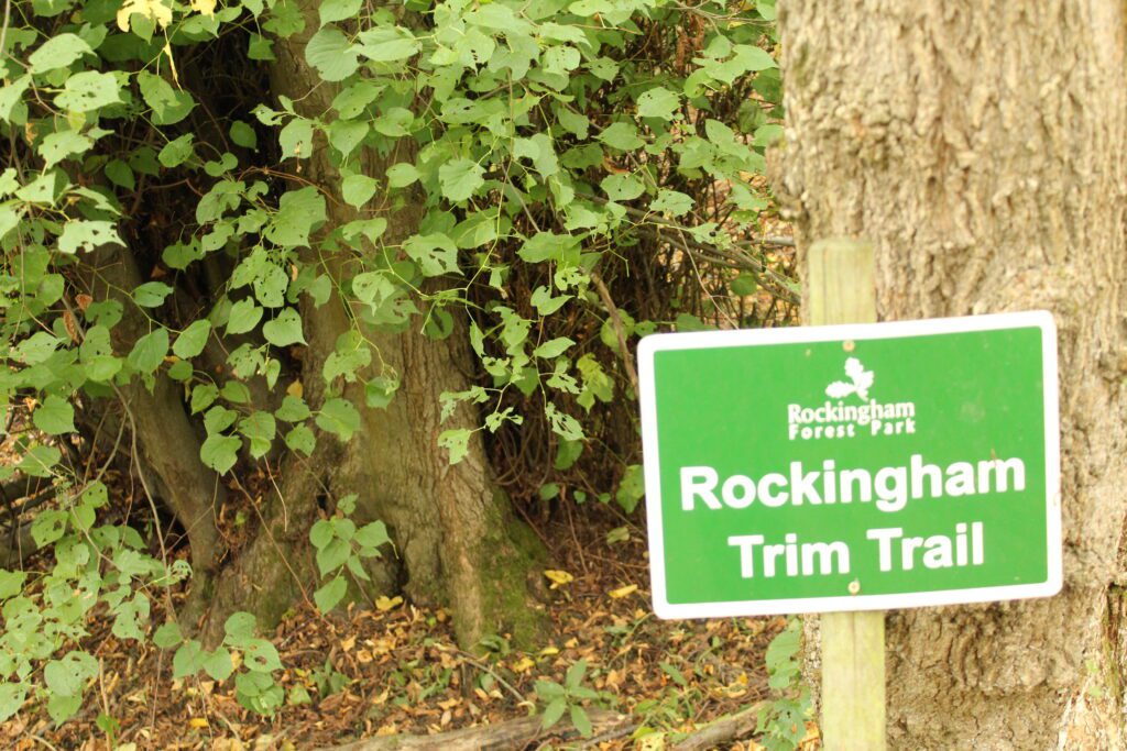A green sign in the woodland reading Rockingham Trim Trail