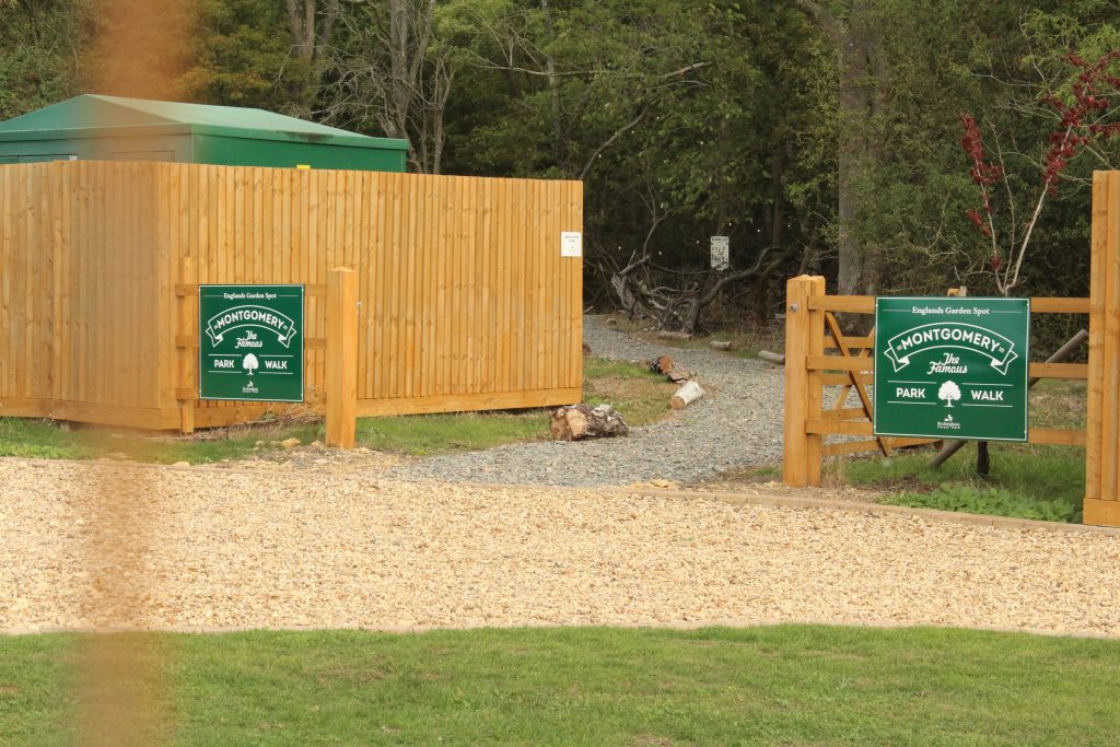 The entrance to the Montgomery Park Walk at Rockingham Forest Park: a gravel path between timber screens, with green waymarker signs either side