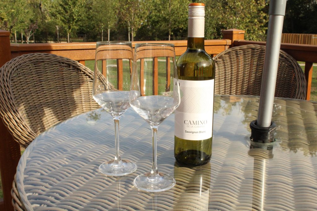 A bottle of wine and two glasses on the table on a lodge deck at Rockingham Forest Park, in late afternoon sun